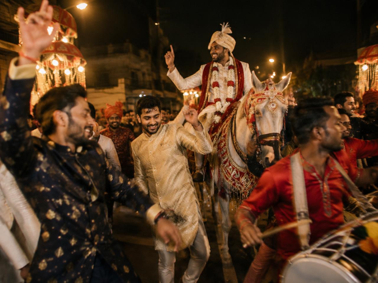 Groom on horseback during a baraat with relatives dancing
